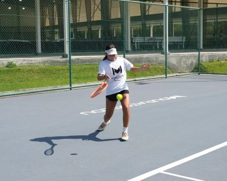 Student hitting a tennis shot on a hard court at Mouratoglou Academy Malaysia on the campus of Epsom College in Malaysia.