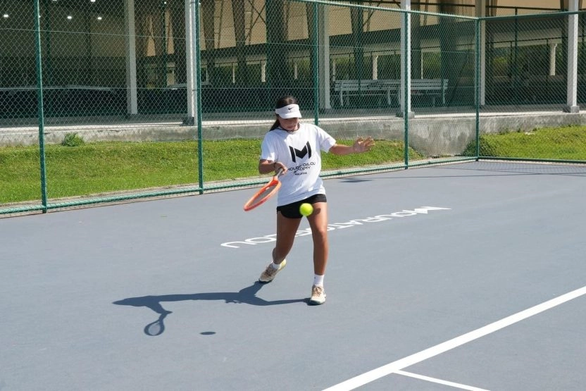 Student hitting a tennis shot on a hard court at Mouratoglou Academy Malaysia on the campus of Epsom College in Malaysia.