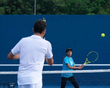 Coach giving a private tennis lesson to a student on an outdoor hard court at Mouratoglou Academy Malaysia on the campus of Epsom College in Malaysia.