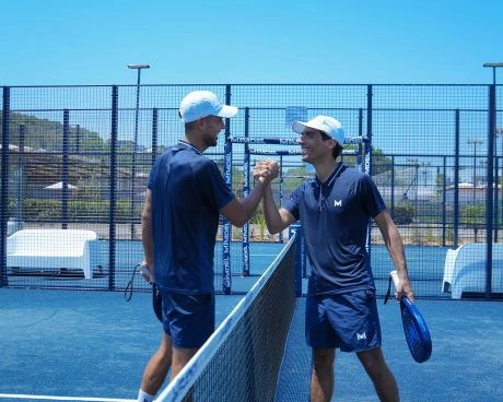 Two padel players shaking hands across the net after a semi-private coaching session on an outdoor padel court.