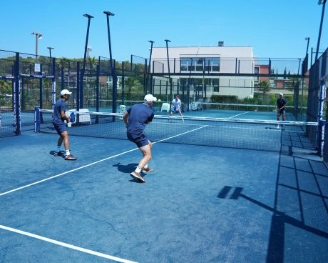 Four players participating in a group padel lesson on an outdoor court, practicing rallies under the guidance of a professional coach.