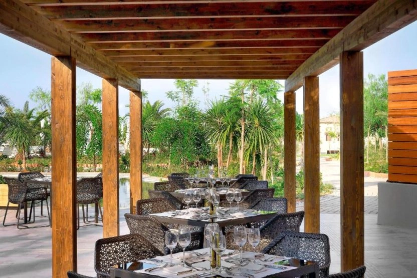 Outdoor restaurant terrace at The Westin Resort Costa Navarino with elegantly set dining tables overlooking landscaped gardens.