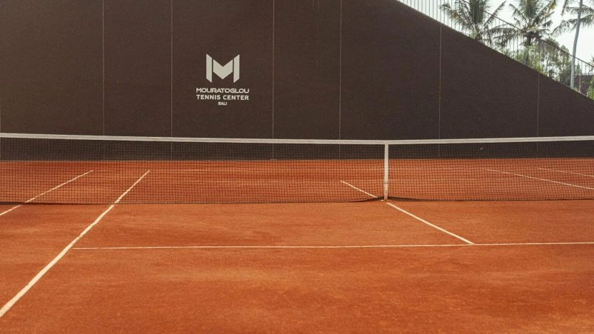 Premium clay tennis court at Mouratoglou Tennis Center Bali with academy branding and tropical surroundings.