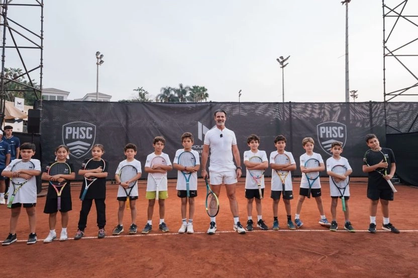 Patrick Mouratoglou posing with a group of young tennis players on a clay court at Mouratoglou Tennis Center Palm Hills Cairo in Egypt.