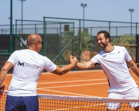 Two tennis players shaking hands at the net after a match on a clay court at Mouratoglou Tennis Center Costa Navarino.