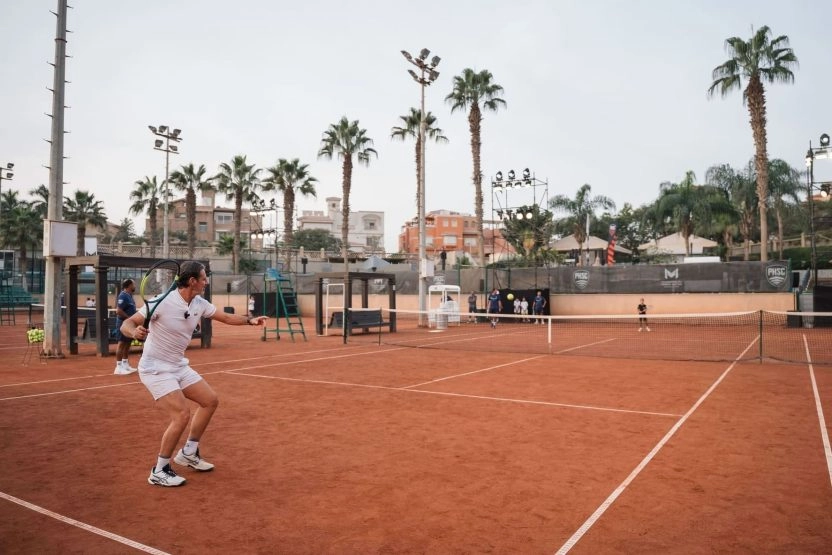 Young girl rallying against Patrick Mouratoglou on a floodlit clay show court at Mouratoglou Tennis Center Palm Hills, Egypt