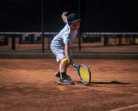 Young tennis player hitting a low forehand on a red clay court at Mouratoglou Academy Rio de Janeiro.