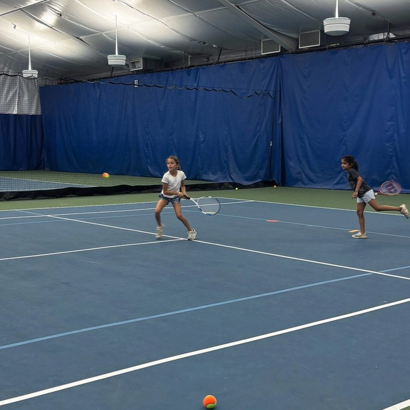 Two young tennis players practicing on an indoor court at Mouratoglou Tennis Center New York.