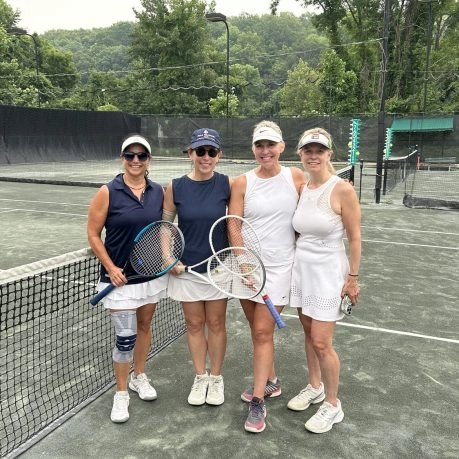 Four women holding tennis rackets and standing together on an outdoor tennis court at Mouratoglou Tennis Center New York.