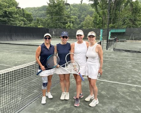 Four women holding tennis rackets and standing together on an outdoor tennis court at Mouratoglou Tennis Center New York.