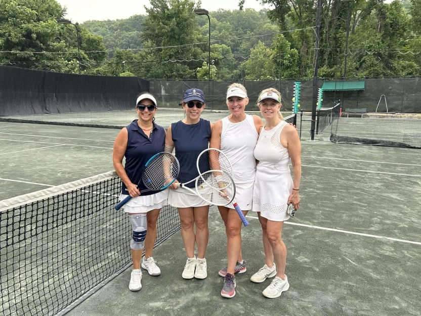 Four women holding tennis rackets and standing together on an outdoor tennis court at Mouratoglou Tennis Center New York.