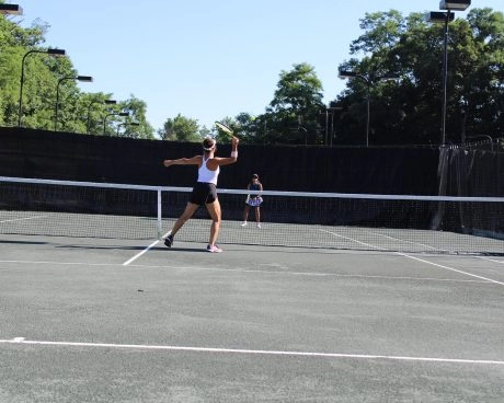 Two players rallying on an outdoor tennis court at Mouratoglou Tennis Center Westchester with trees and fencing behind them.