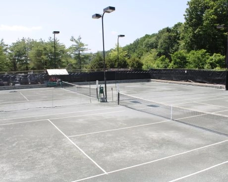 Empty outdoor tennis courts at Mouratoglou Tennis Center Westchester with fencing, court lights, and trees in the background.
