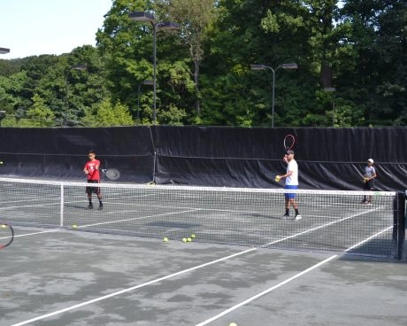 Tennis players practicing on an outdoor court at Mouratoglou Tennis Center Westchester with trees and fencing in the background.