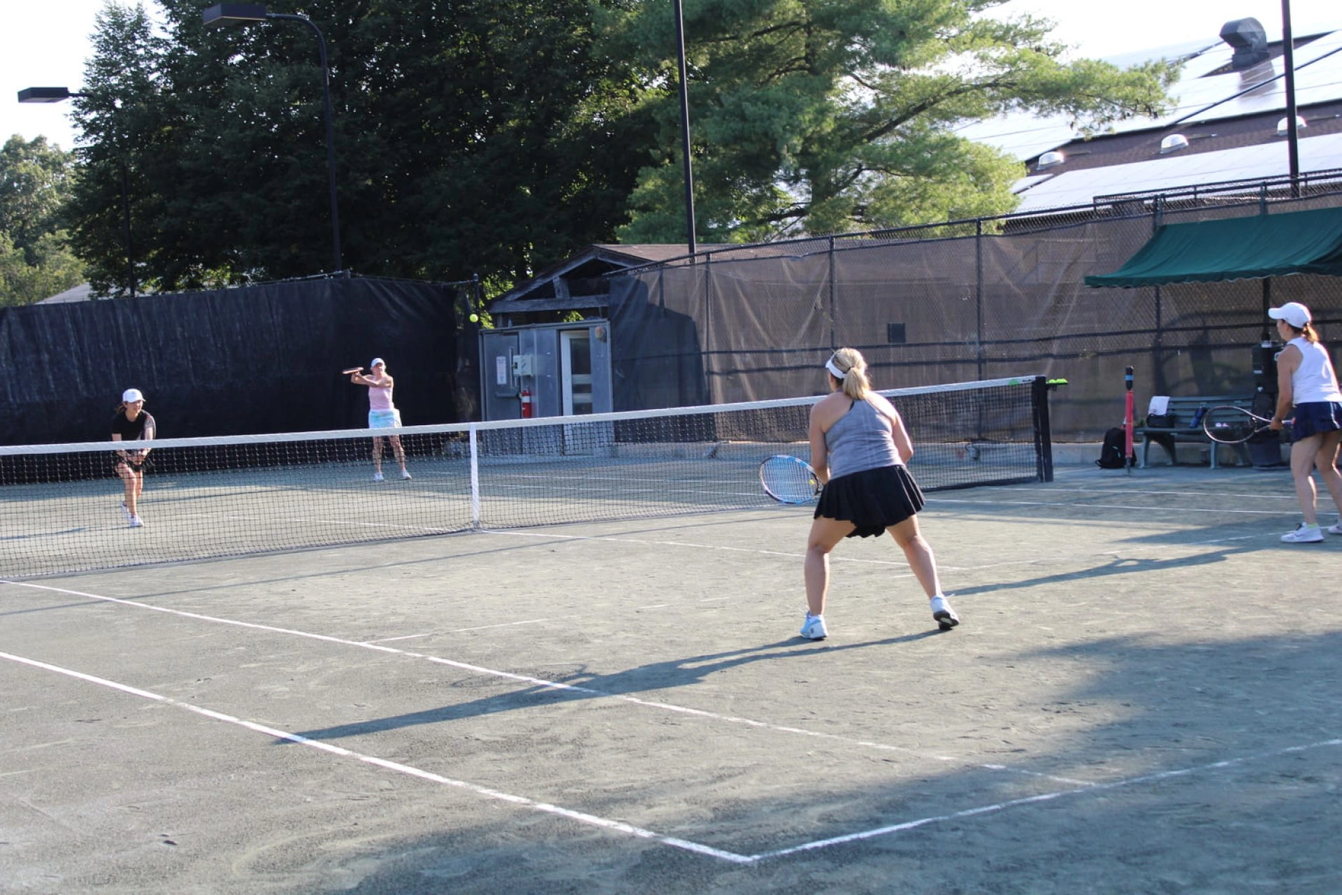 Adult players playing doubles on an outdoor tennis court at Mouratoglou Tennis Center New York.