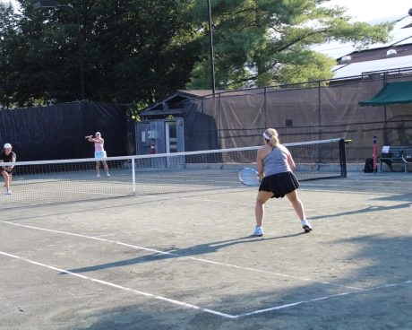Adult players playing doubles on an outdoor tennis court at Mouratoglou Tennis Center New York.