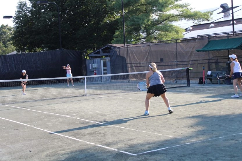 Adult players playing doubles on an outdoor tennis court at Mouratoglou Tennis Center New York.