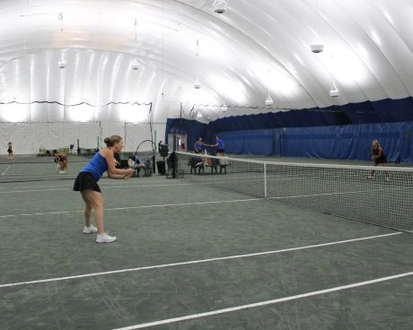 Adult players playing tennis on indoor courts under a white dome at Mouratoglou Tennis Center New York.