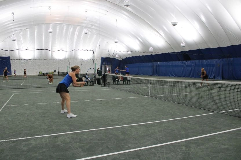 Adult players playing tennis on indoor courts under a white dome at Mouratoglou Tennis Center New York.
